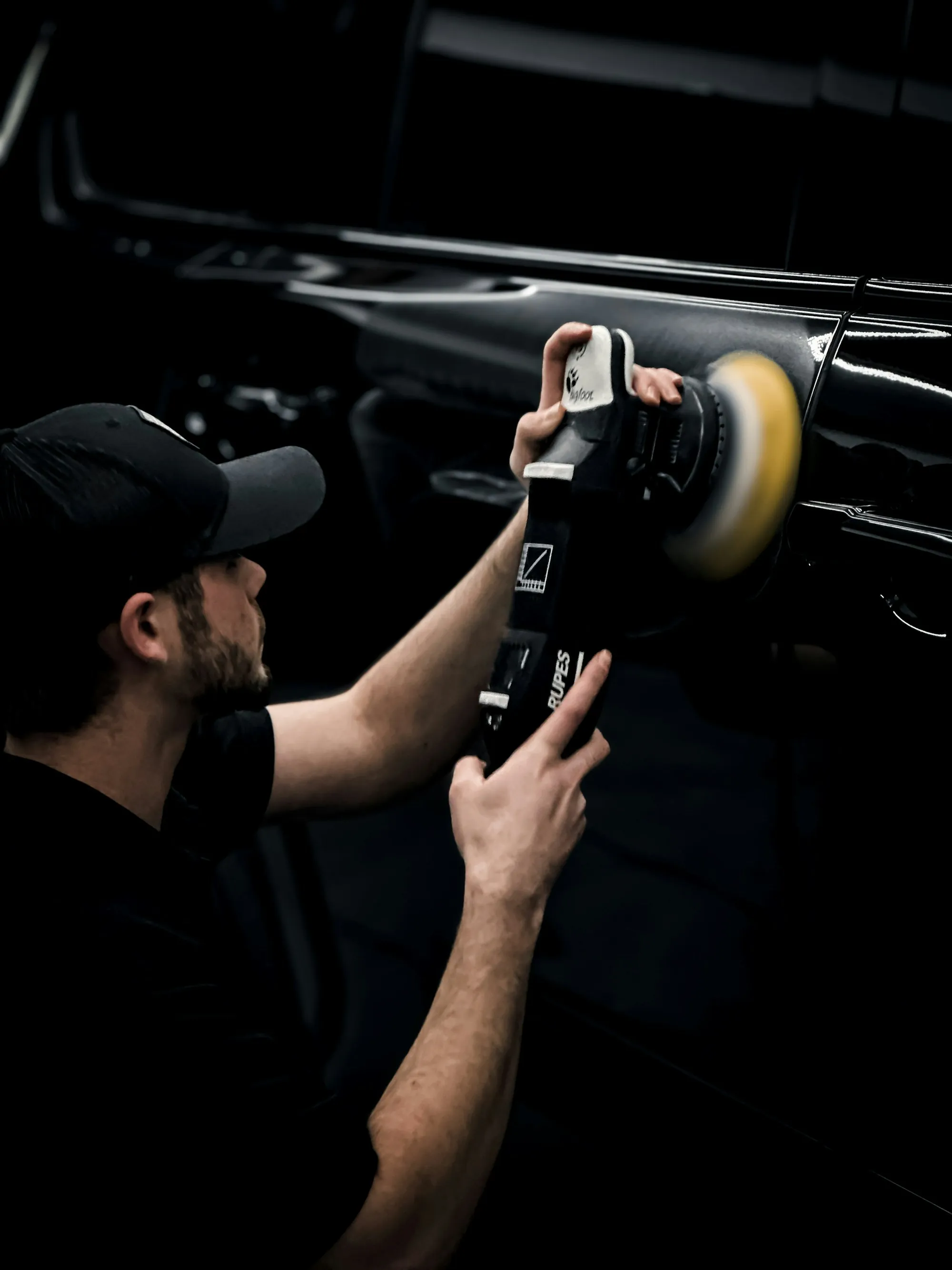 Technician polishing a car panel in a dark garage
