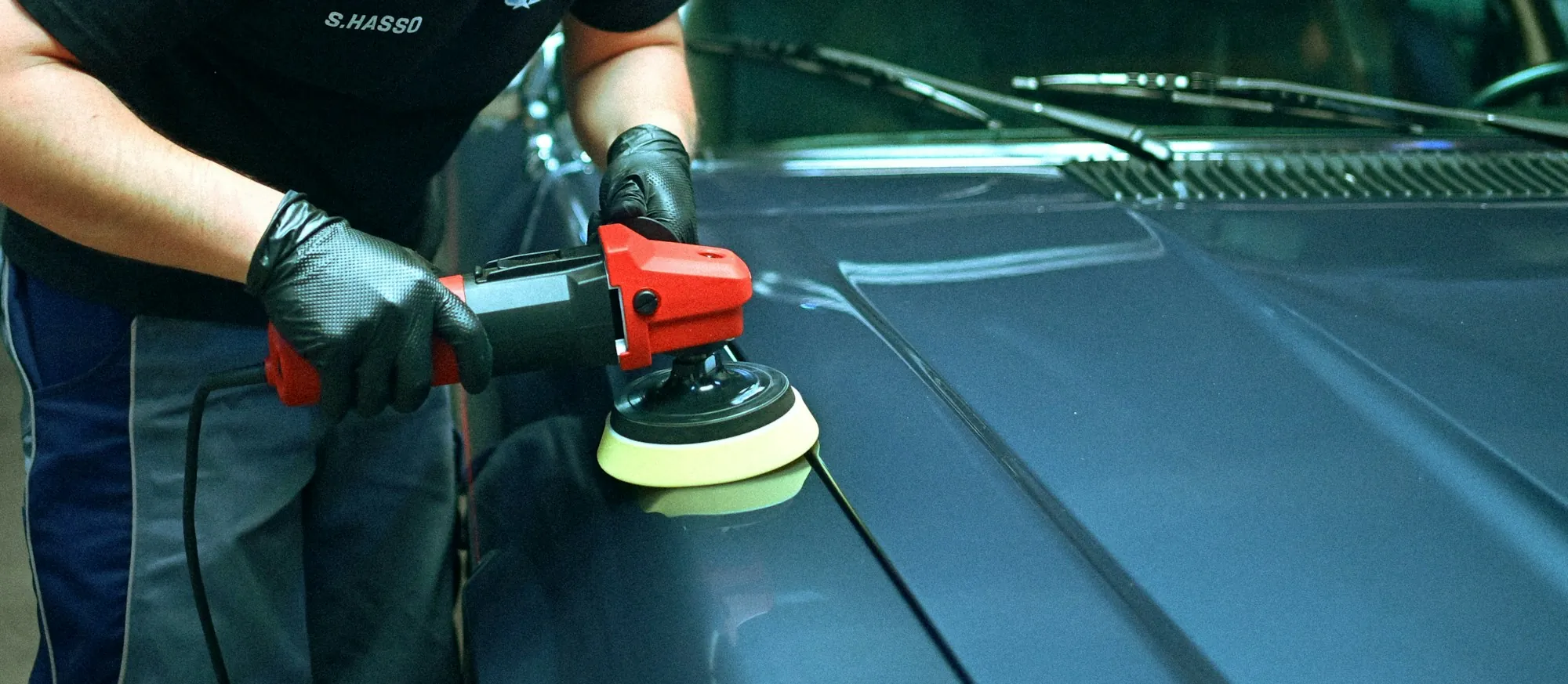 Gloved hands machine polishing the hood of a teal car